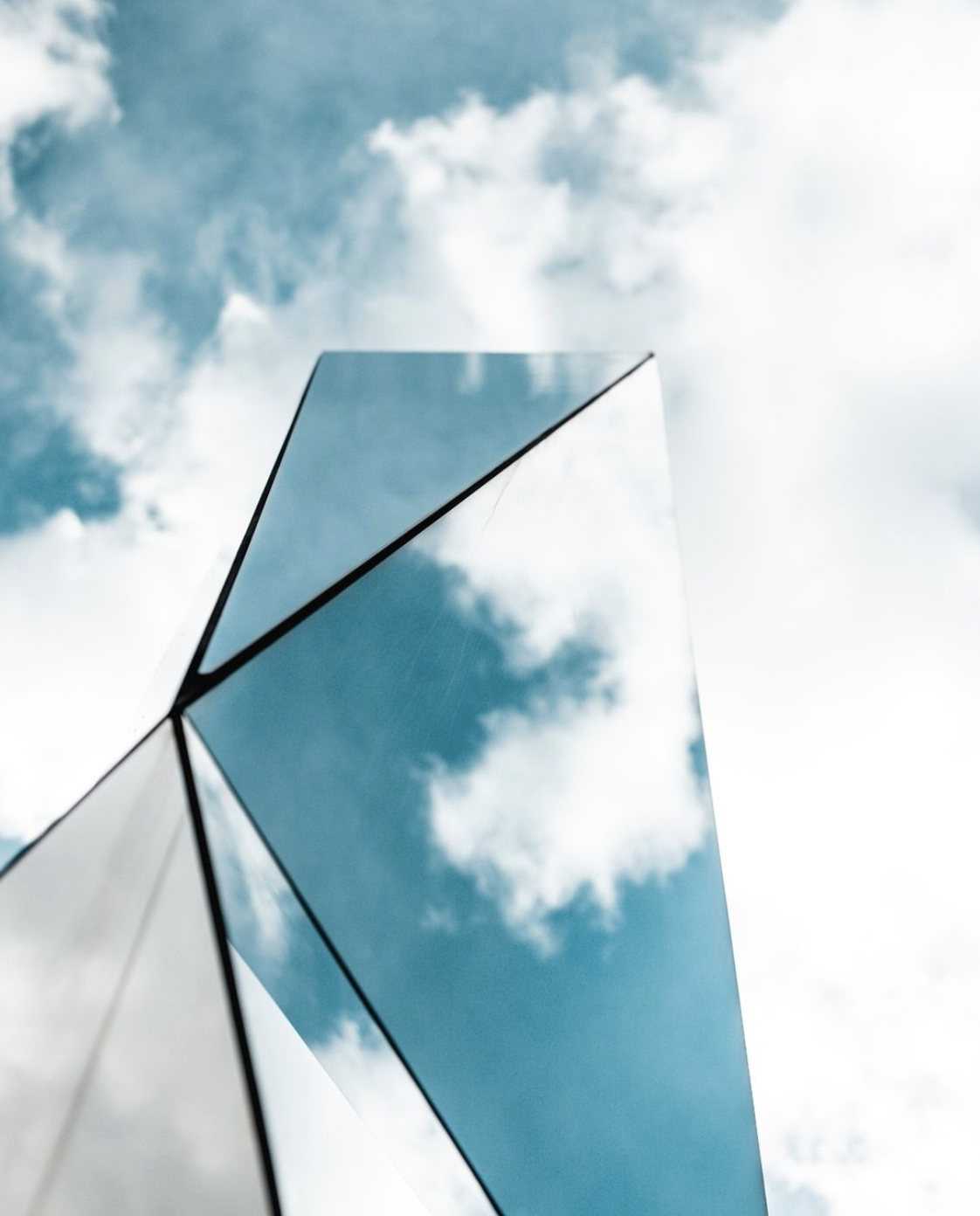 A mirrored shape reflects clouds in the sky.