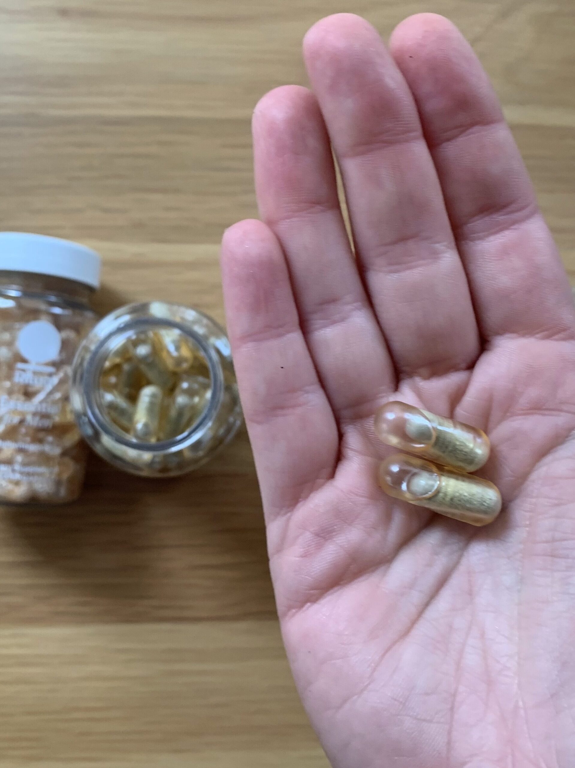 A hand holding two capsules of Ritual prenatal vitamins.