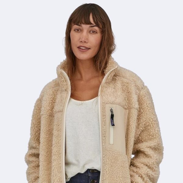 A person wearing a beige fleece jacket and a white top stands against a plain background.