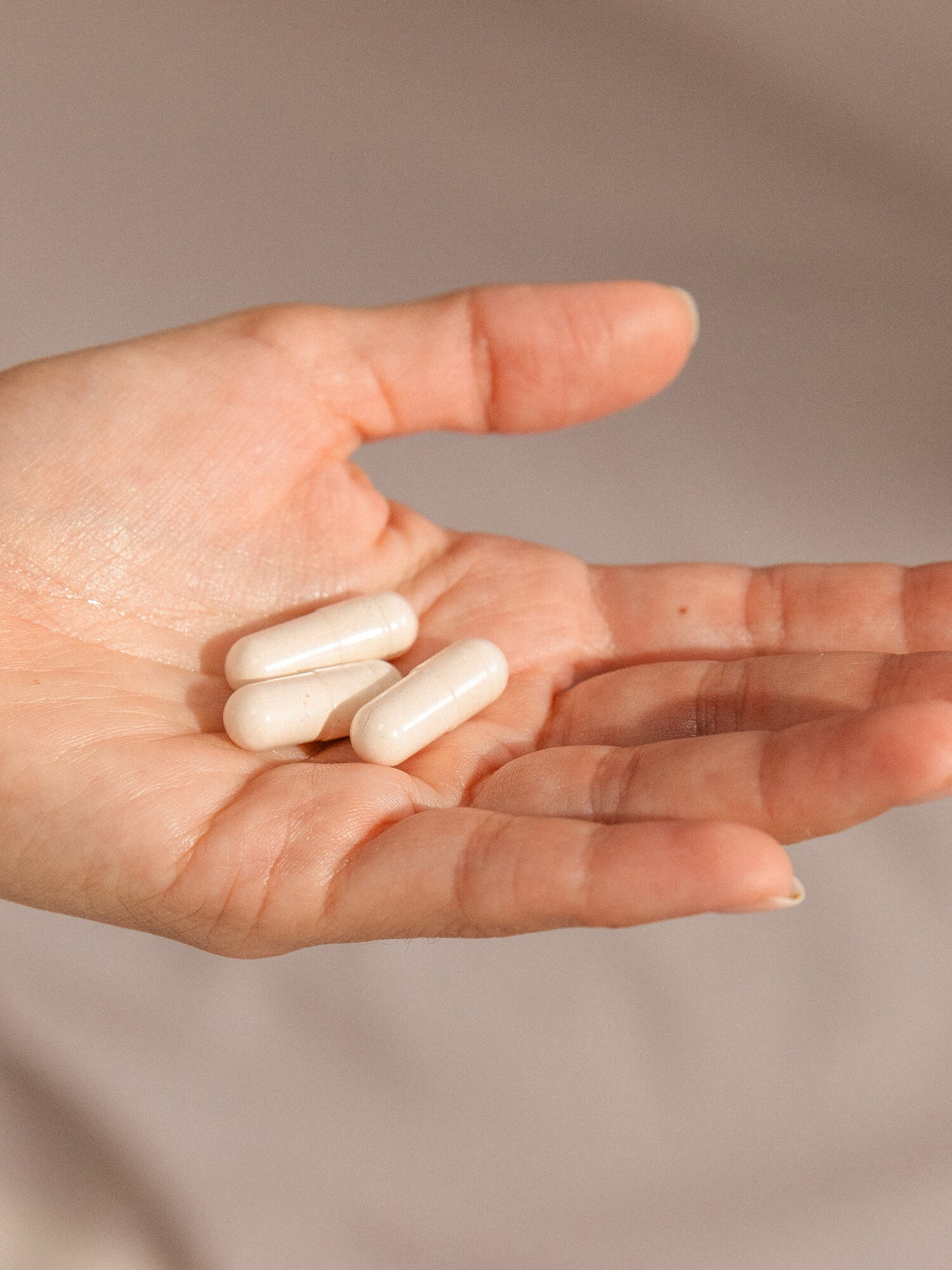 A hand holding three Needed Multivitamin capsules. 