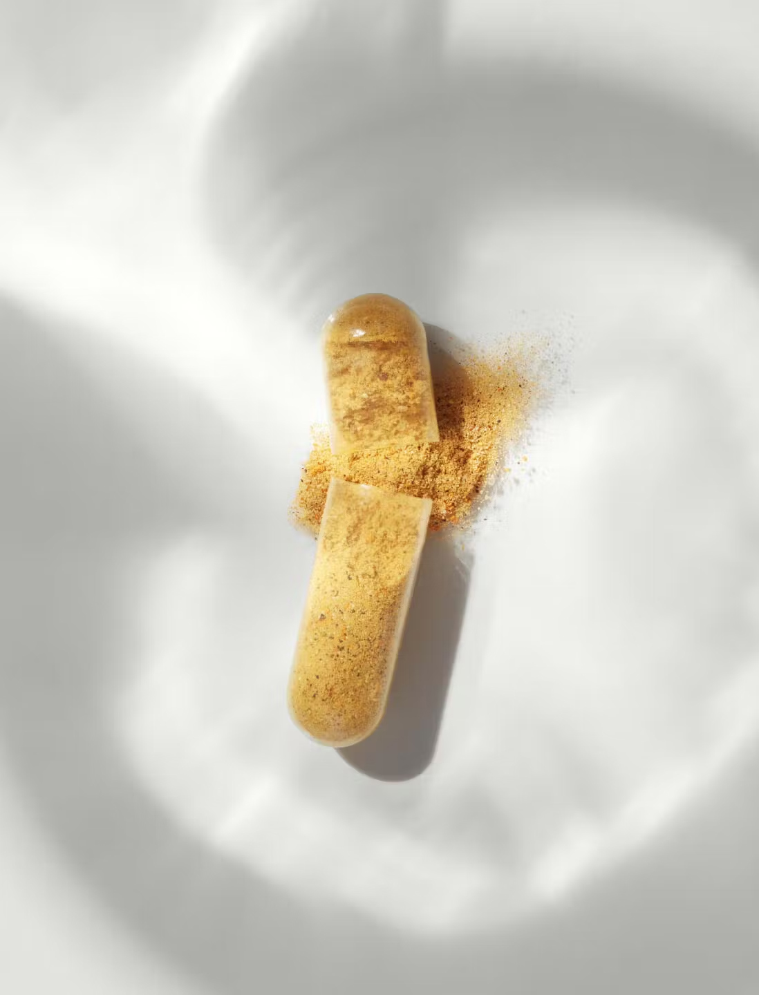 A close up of a capsule broken open to show the powder inside spilling out.