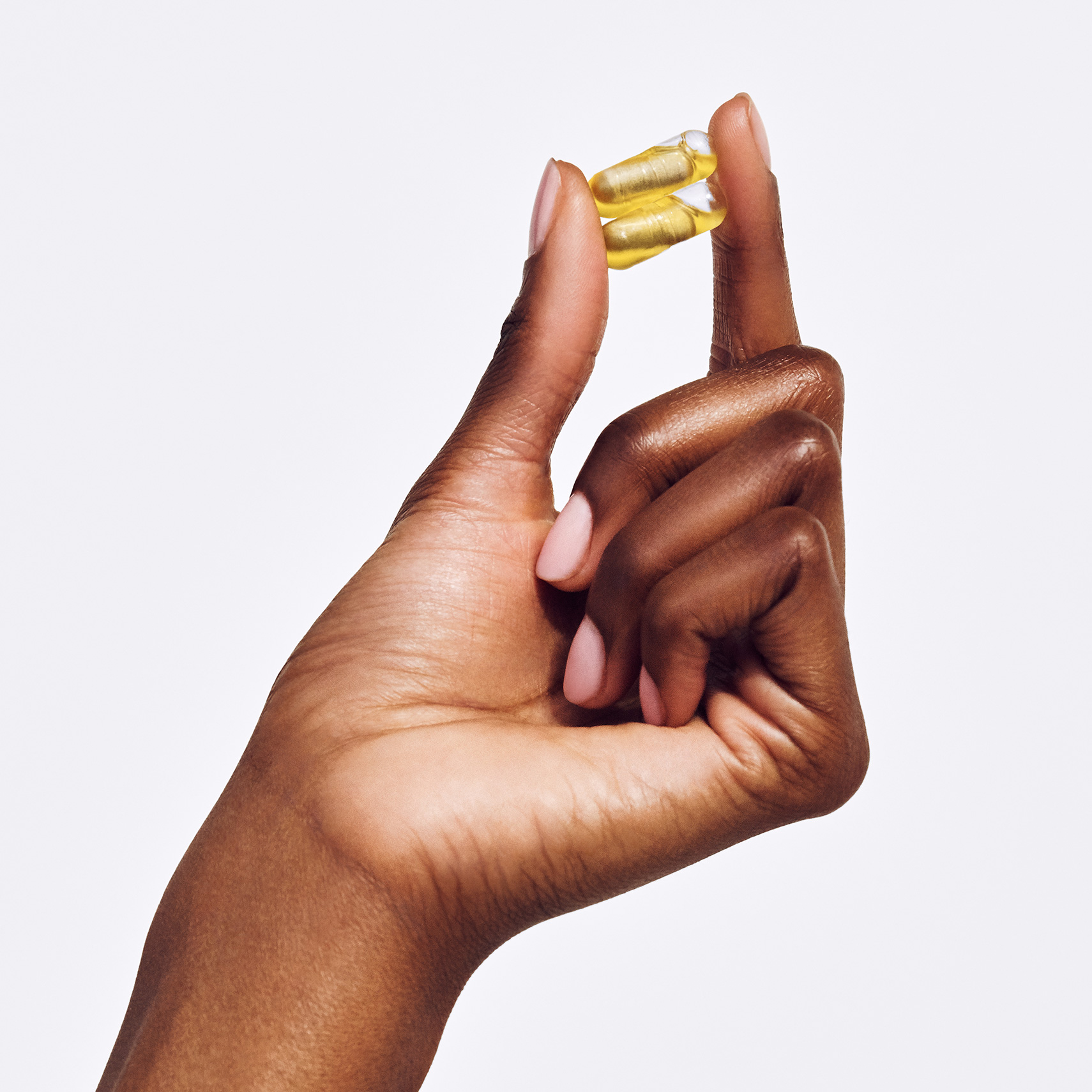A hand holds two Ritual postnatal vitamin capsules.