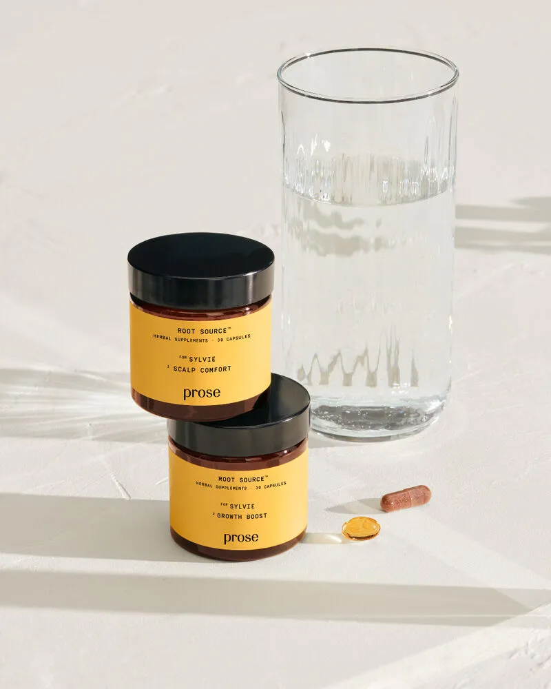 Two Prose supplement jars stacked next to a glass of water. A pill from each type lies next to them.