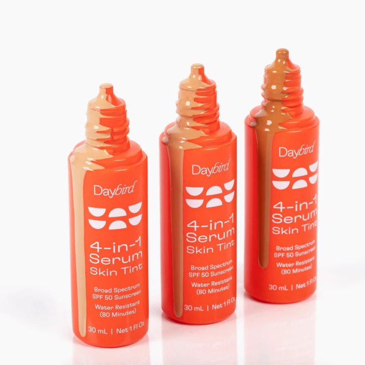 Three orange bottles of Daybird 4-in-1 Serum Skin Tint with SPF 50 sunscreen, each with a different shade of tint visible from the opening. Bottles are 30 mL (1 fl oz) each.