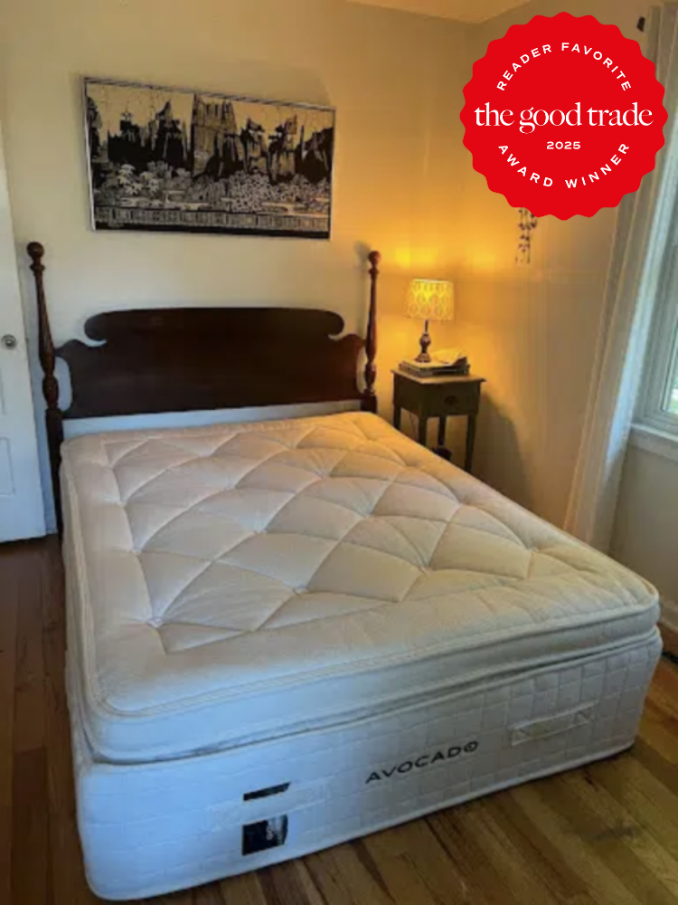 Bedroom with a wooden bed frame, a large mattress labeled "Avocado," a side table with a lamp, and a wall art piece. A red badge in the corner reads "FashionGroomSpot 2025 Reader Favorite Award Winner.