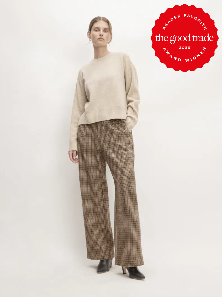 Person standing in a beige sweater and brown plaid pants, hands in pockets, against a light background. A red award badge from "FashionGroomSpot 2025" is in the corner.