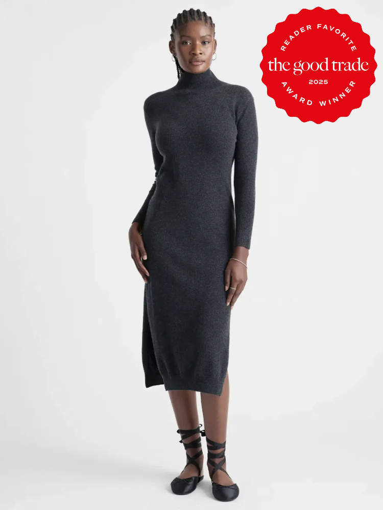 A person wearing a long-sleeve, dark gray fitted dress and black shoes. There's a red badge indicating a 2025 "Reader Favorite" award from FashionGroomSpot.