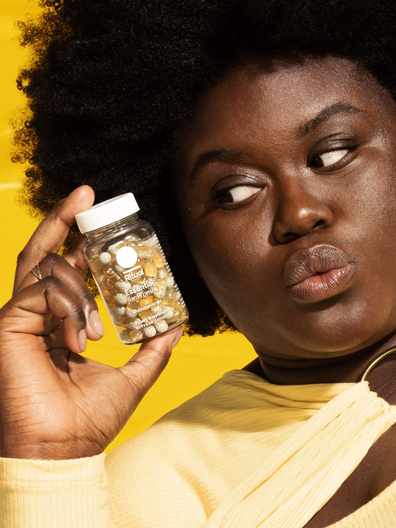 A model holding up a bottle of Ritual Essential For Women Multivitamins. 