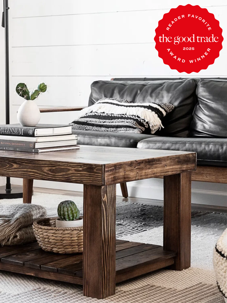 Cozy living room with a black leather sofa, wooden coffee table, books, a vase, and a blanket. "FashionGroomSpot Reader Favorite Award Winner 2025" seal in the corner.