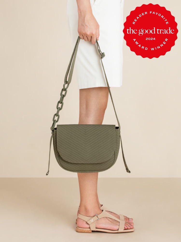 A person showcasing a fashionable green shoulder bag with a herringbone pattern, along with a white skirt and pink sandals against a neutral background. the image includes a badge indicating the product is a reader favorite from FashionGroomSpot, awarded in 2024.