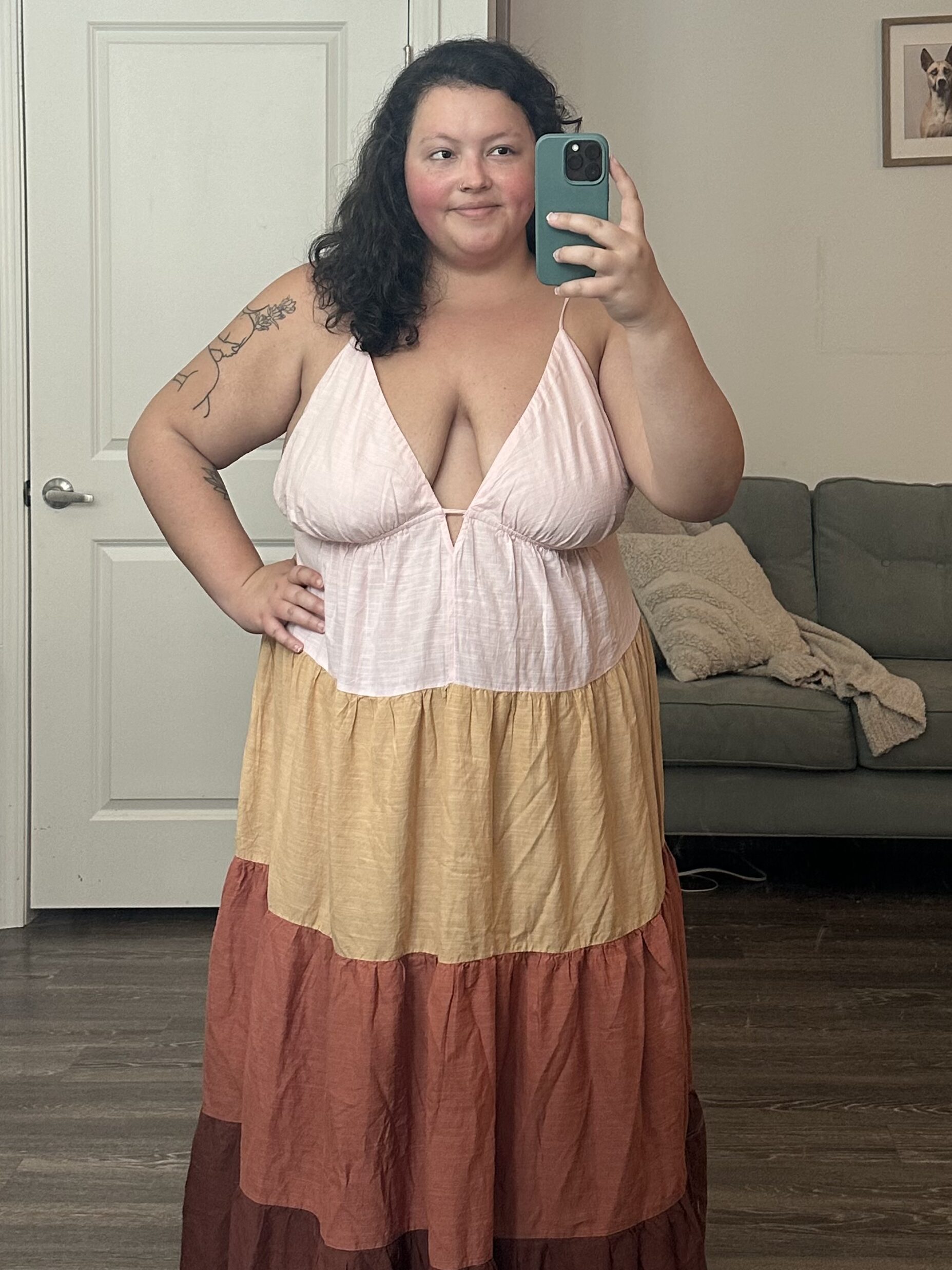 Woman in a multi-colored maxi dress taking a selfie with her phone in a mirror.