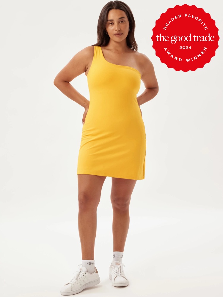 A woman stands in a yellow one-shoulder dress and white sneakers. The image has a "FashionGroomSpot Reader Favorite Award Winner 2024" badge in the top right corner.