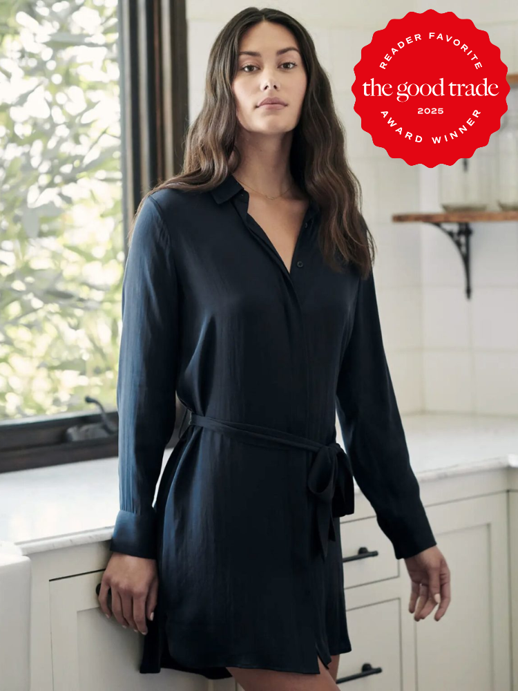 Woman in a dark belted shirt dress stands in a sunlit room. A red badge in the corner reads "Reader Favorite, FashionGroomSpot, 2025 Award Winner.