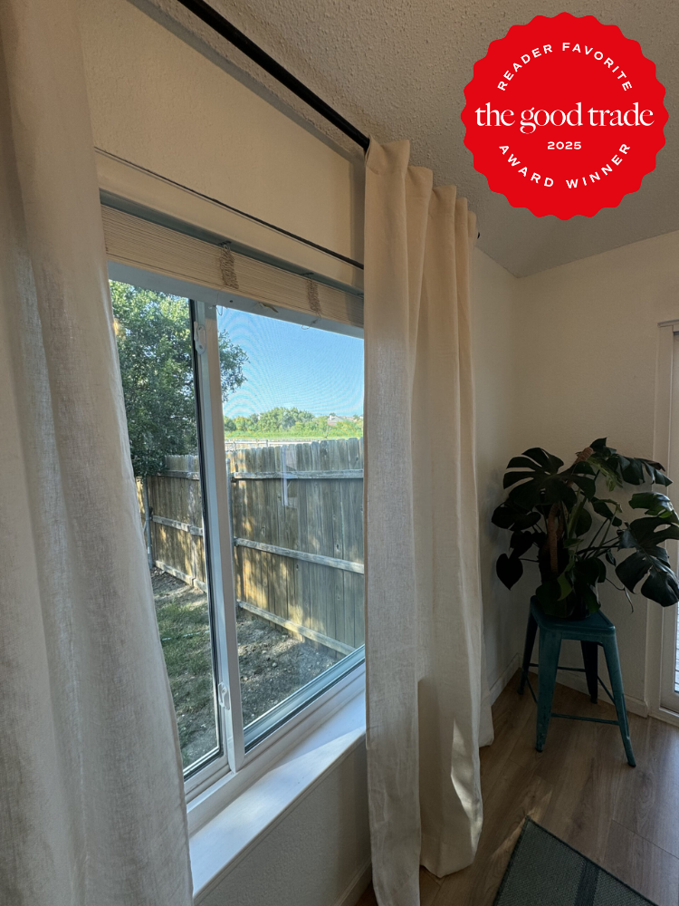 Room with a window covered by white curtains, a wooden floor, and a plant on a green stool. There's an award badge for "FashionGroomSpot 2025" on the top right corner.