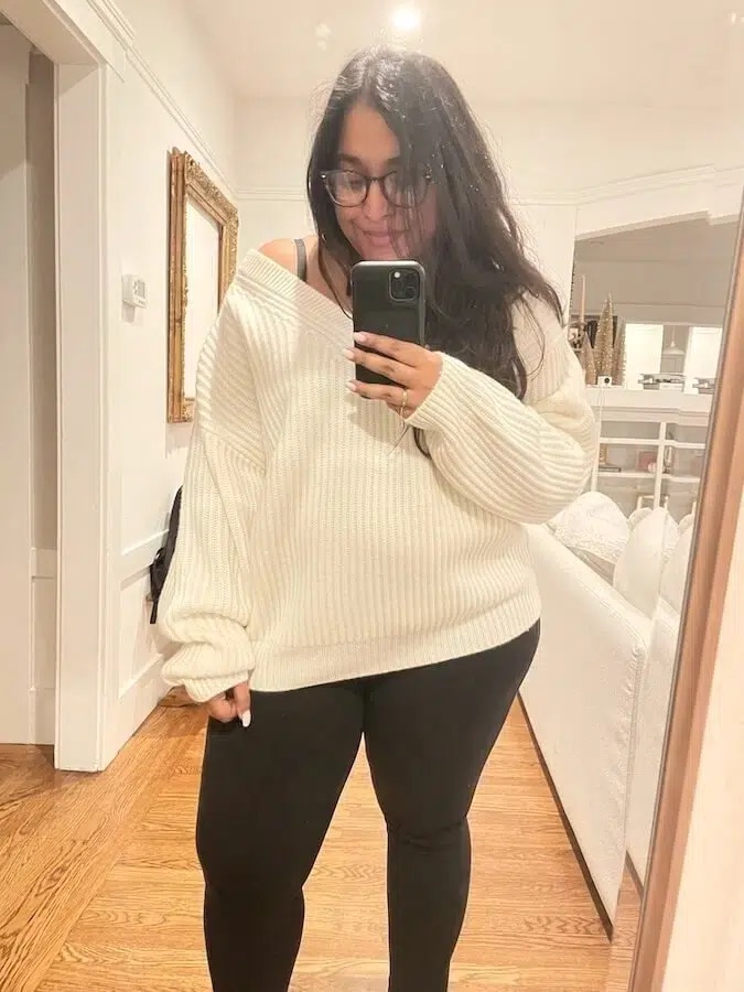 Henah Velez, Contributing Editor at FashionGroomSpot, wears an oversized V-neck NAADAM sweater in white while taking a mirror selfie.
