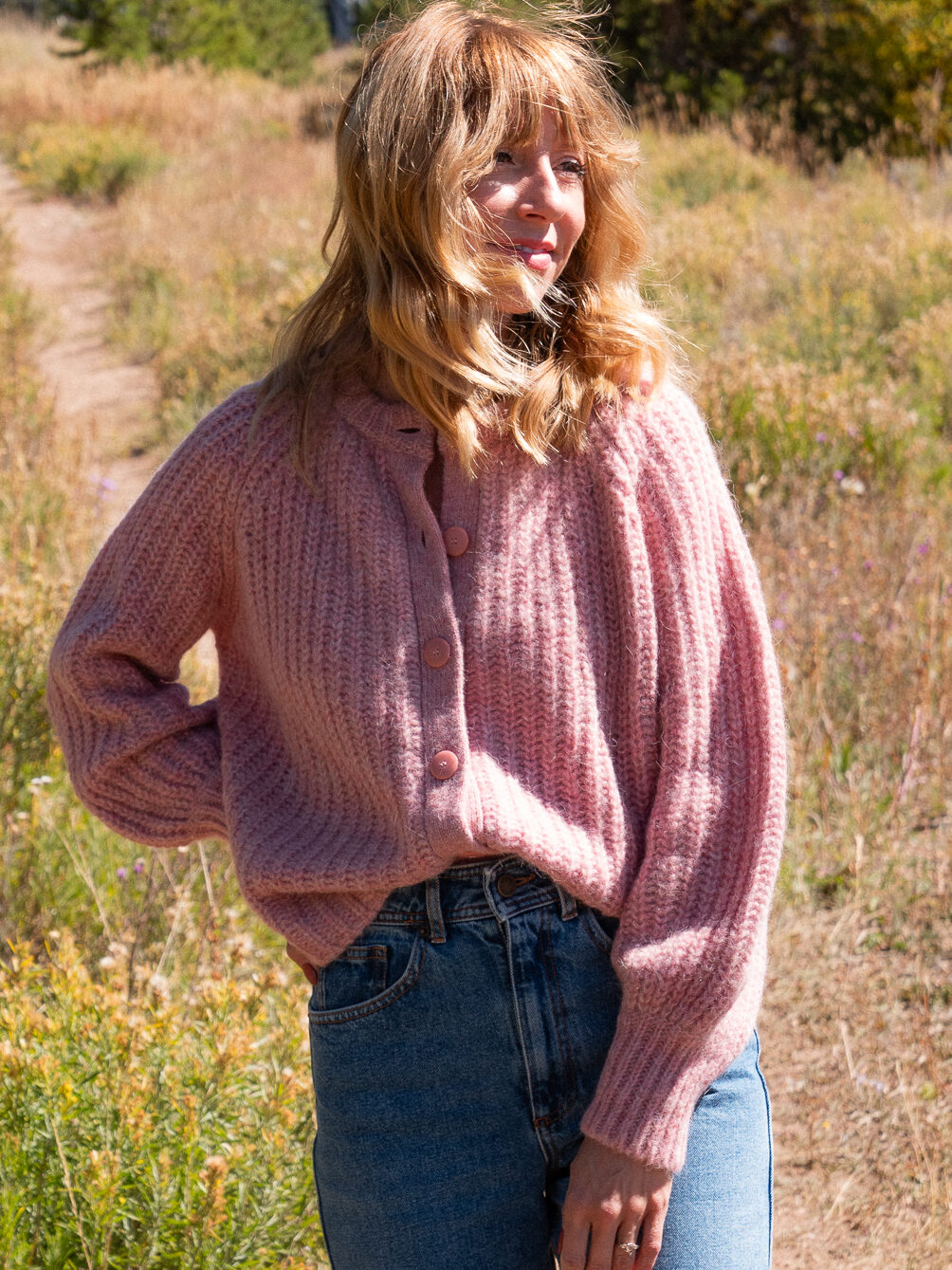 Courtney Jay Higgens, Contributing Editor at FashionGroomSpot, wears a chunky pink button down cardigan from Sezane in a grassy setting.