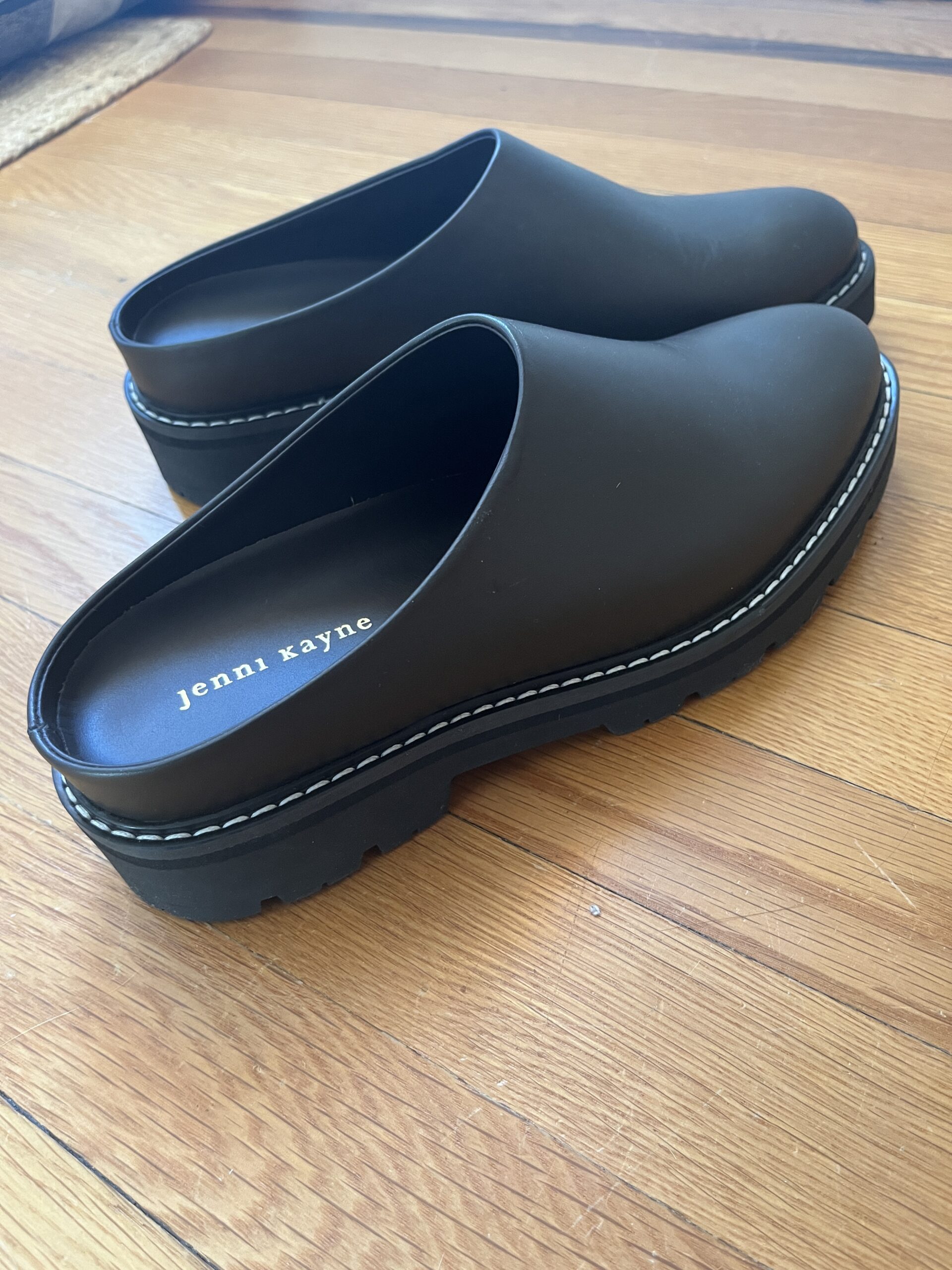 A close up of black lug mules with Jenni Kayne embossed in gold in the sole.