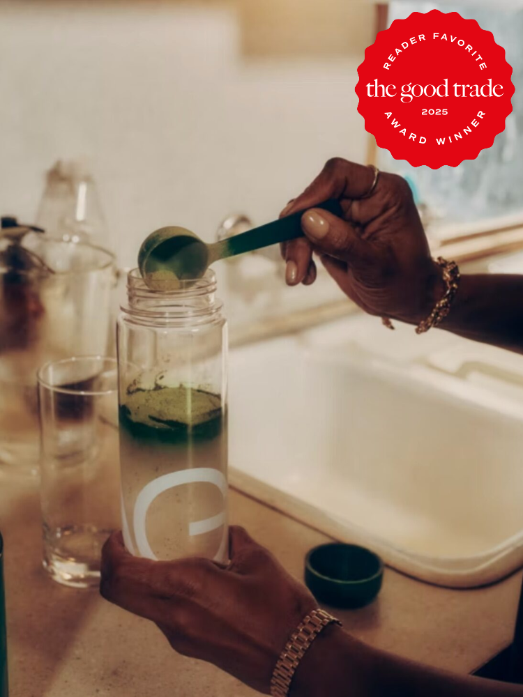 Person adding green powder to clear water bottle on kitchen counter; "FashionGroomSpot 2025 award winner" badge in the top right corner.