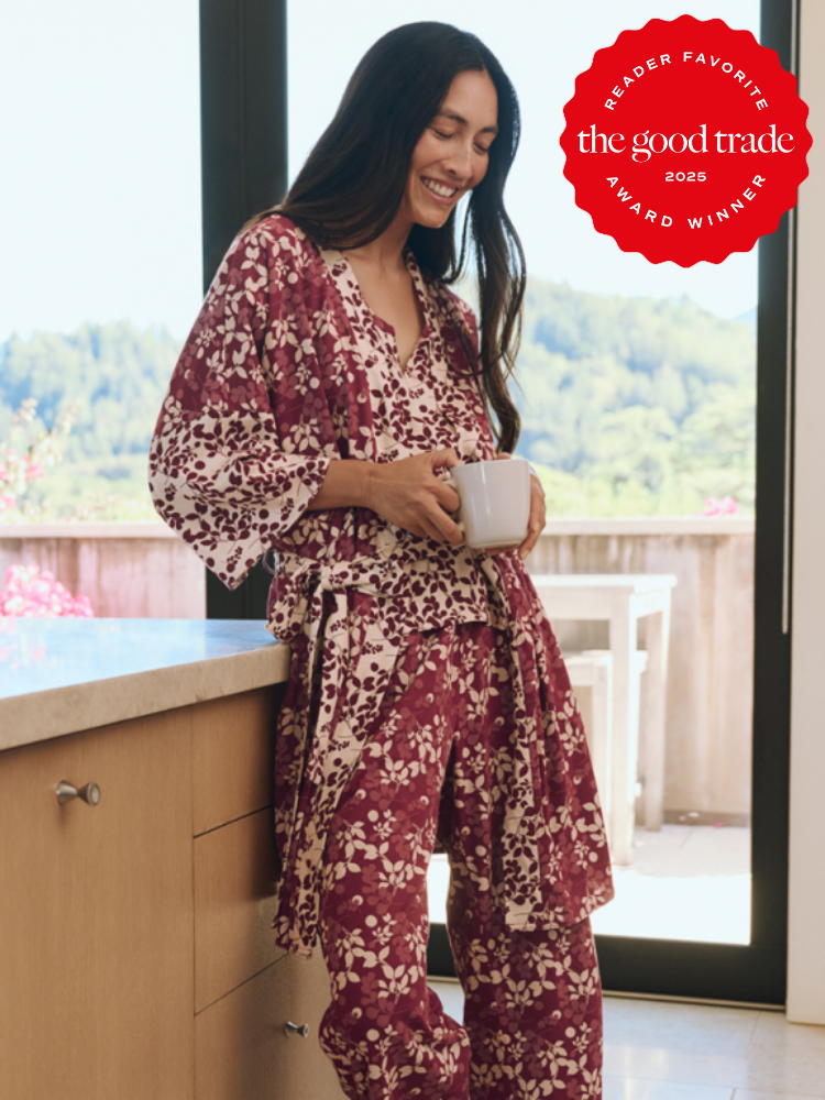 Woman in floral pajamas stands by a kitchen counter holding a mug, with a "FashionGroomSpot" award badge in the corner.