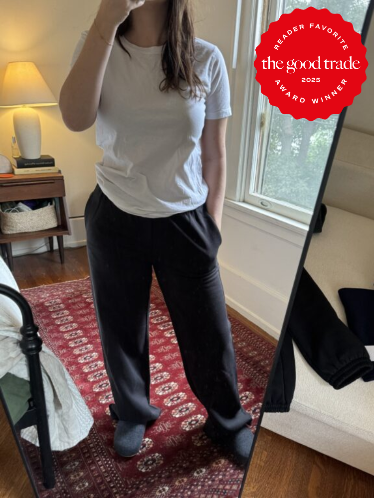 Person in white t-shirt and black pants takes mirror selfie in a room. A red award badge from "FashionGroomSpot 2025" is placed on the image.