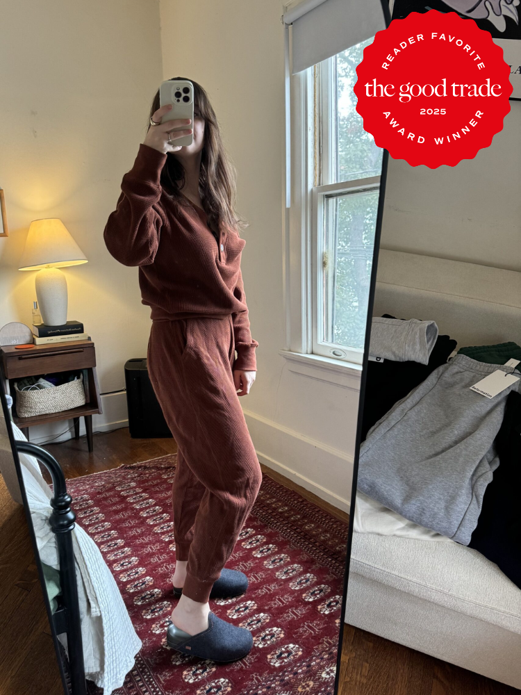 Person taking a mirror selfie in a bedroom, wearing a brown outfit and slippers. A red award badge is displayed in the top right corner.
