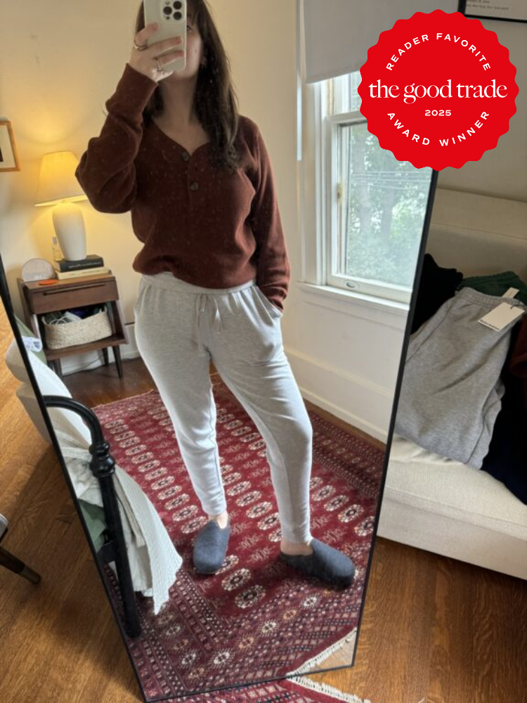Person takes a mirror selfie in a bedroom, wearing a brown sweater, gray sweatpants, and slippers. A "FashionGroomSpot 2025 Reader Favorite Award Winner" badge is in the corner.