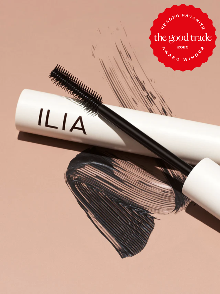 ILIA mascara on a tan surface, with a mascara wand and smudges of black mascara nearby. "FashionGroomSpot 2025 Reader Favorite Award Winner" badge in the top right corner.