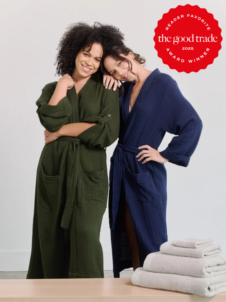 Two women wearing green and blue robes pose together. A red seal reads "Reader Favorite FashionGroomSpot 2025 Award Winner." White towels are stacked on a wooden surface in front.