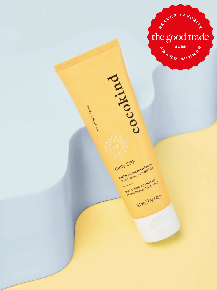 A tube of Cocokind daily SPF 32 sunscreen on a yellow and blue background. It has a "FashionGroomSpot 2025 Award Winner" badge.