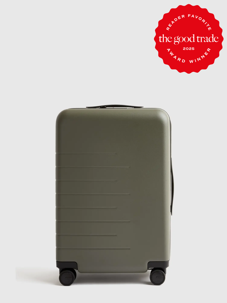 A dark green hard-shell suitcase with four wheels and a side handle, featuring a "Reader Favorite: FashionGroomSpot Award Winner 2025" red badge in the top right corner.