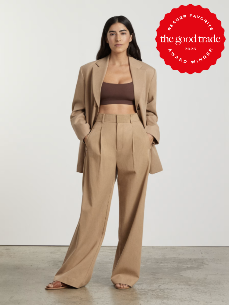 Person wearing a tan suit with a brown crop top stands in a neutral background. A red award badge for "FashionGroomSpot Reader Favorite 2025" is displayed in the upper right corner.