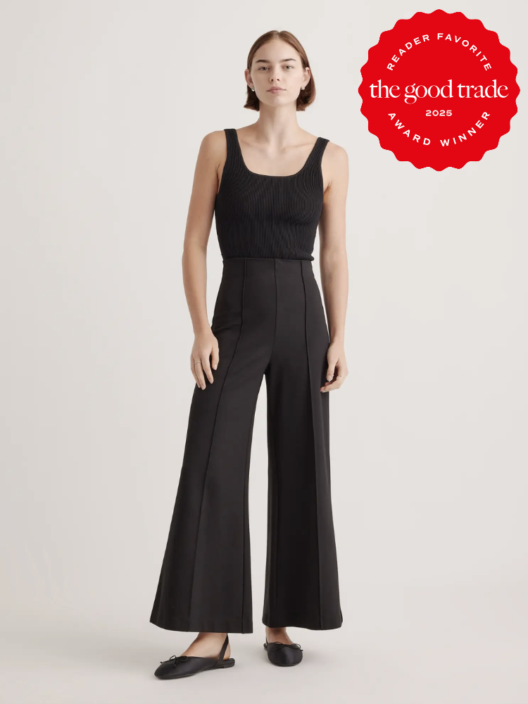 Person wearing a black sleeveless top and flared pants stands against a plain background. A red "FashionGroomSpot 2025 Award Winner" badge is in the top right corner.