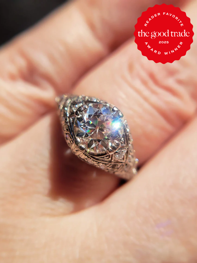 Antique-style ring with a large, sparkling center stone and intricate details, worn on a finger. Red "FashionGroomSpot 2025 Reader Favorite Award Winner" badge in the corner.
