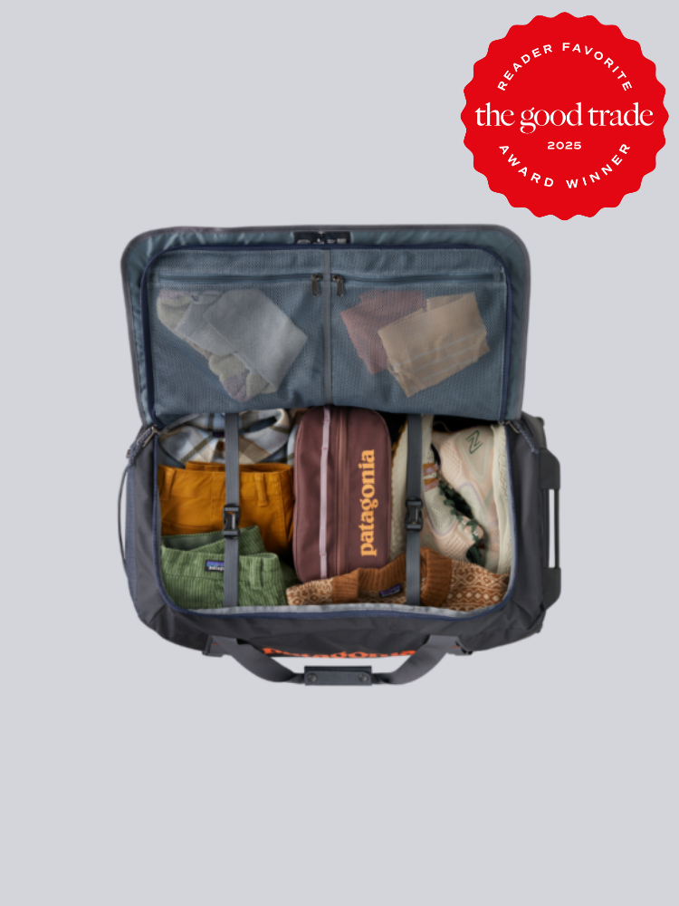 Open travel bag showing neatly packed clothing, shoes, and accessories. Red "FashionGroomSpot 2025 Award Winner" badge at the top right corner.