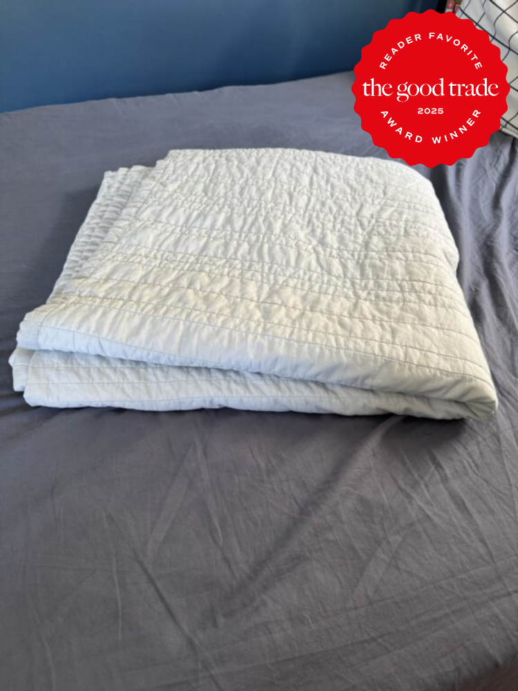 A folded, white quilt lies on a bed with gray sheets. A red badge in the top right corner reads "Reader Favorite, FashionGroomSpot, Award Winner, 2025.