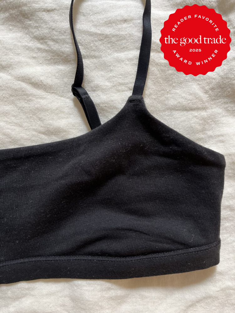 A black bralette with thin straps lays on a light fabric surface. A red badge in the corner reads "Reader Favorite FashionGroomSpot Award Winner 2025.