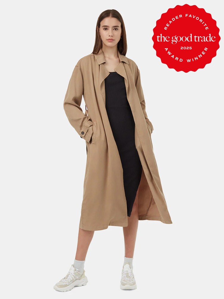 Woman in a black dress and beige trench coat poses in sneakers. Red badge reads "Reader Favorite, FashionGroomSpot, Award Winner 2023.