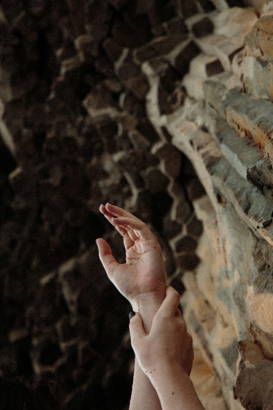 Hands reaching upward towards a textured rocky surface in a dimly lit environment.