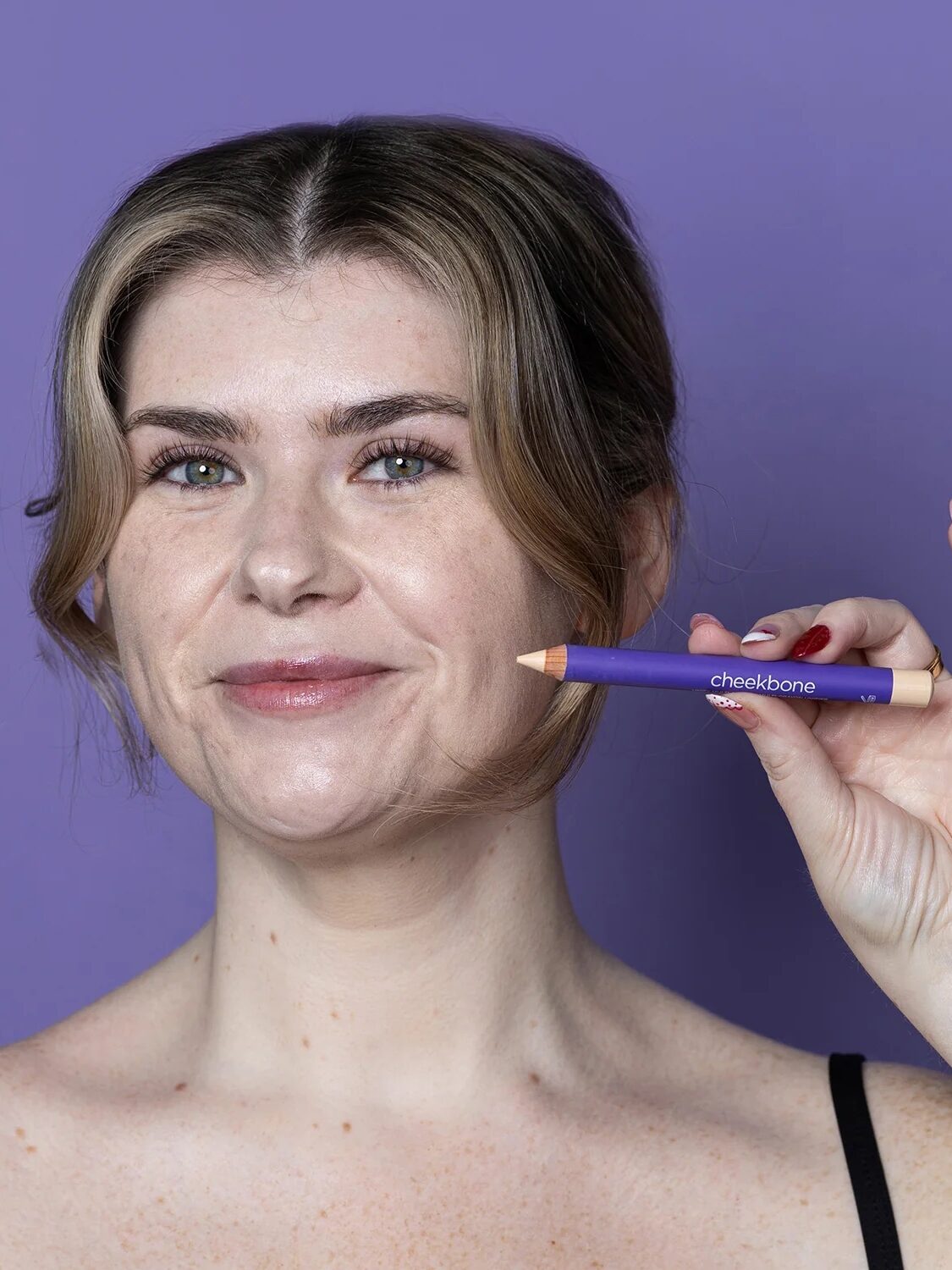 Person holding a purple makeup product labeled "cheekbone" against a matching purple background.