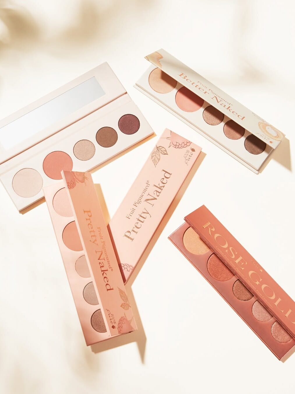 Various makeup palettes with shades of pink, brown, and gold are arranged on a light surface.