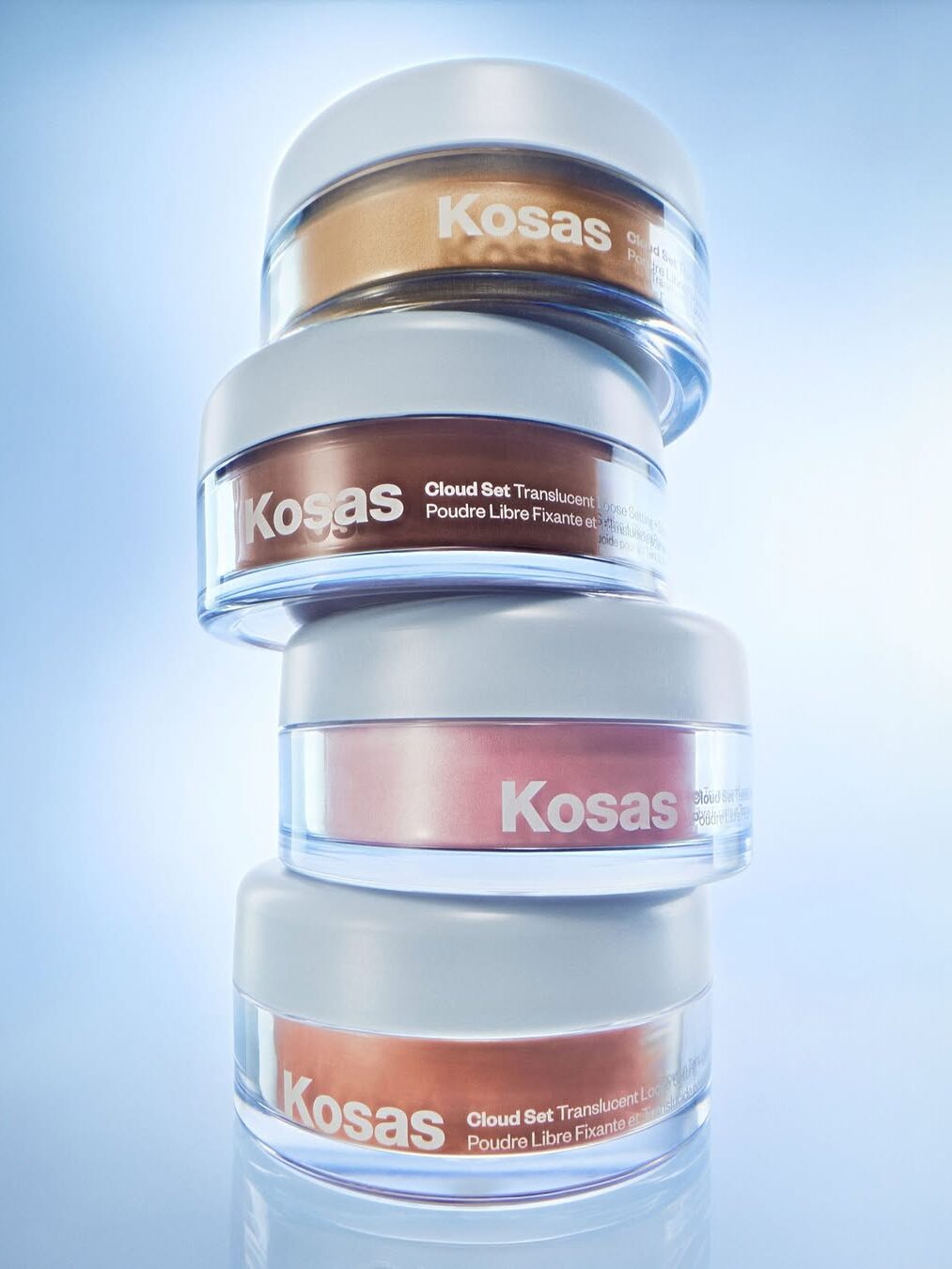 Four stacked Kosas Cloud Set translucent powder containers in frosted glass jars, photographed with a blue gradient background.