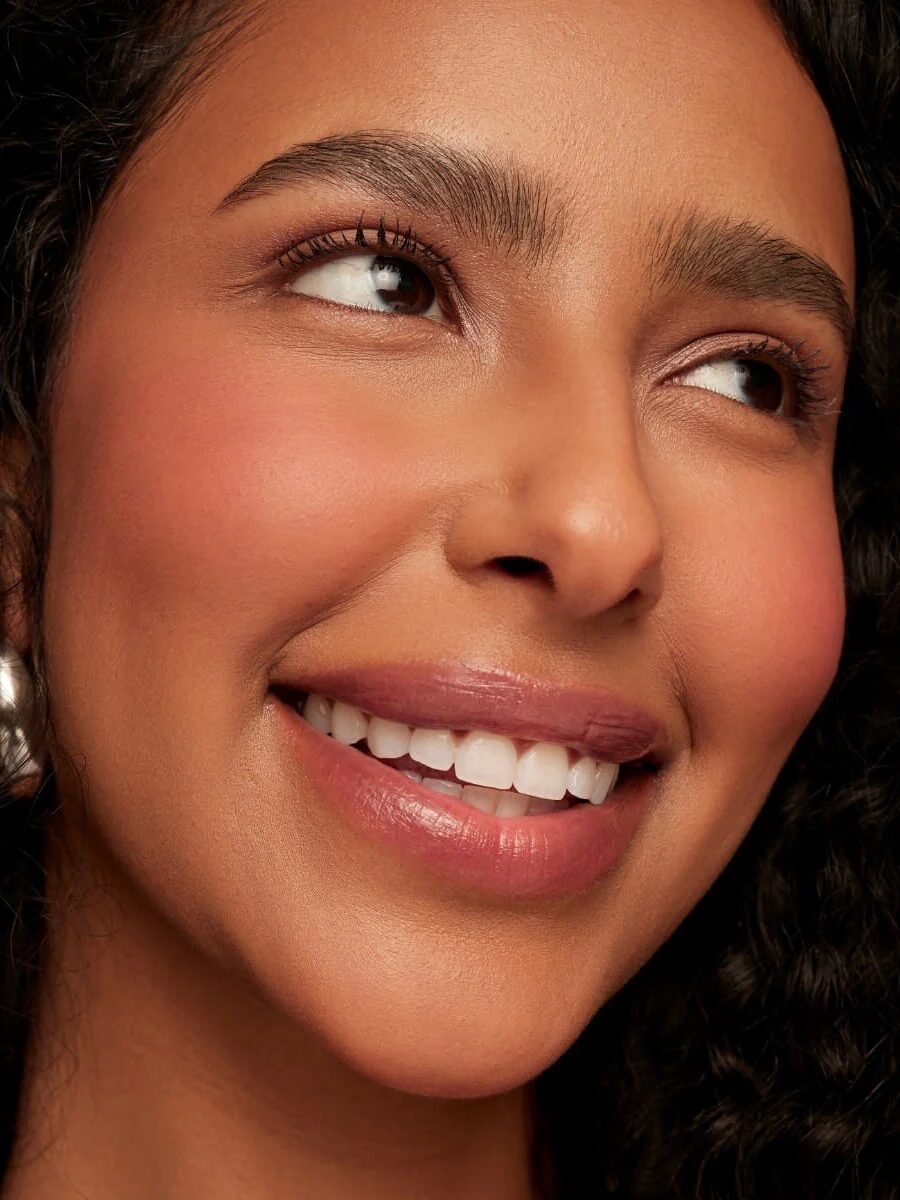 A person with curly hair smiles while looking upward, showing teeth.