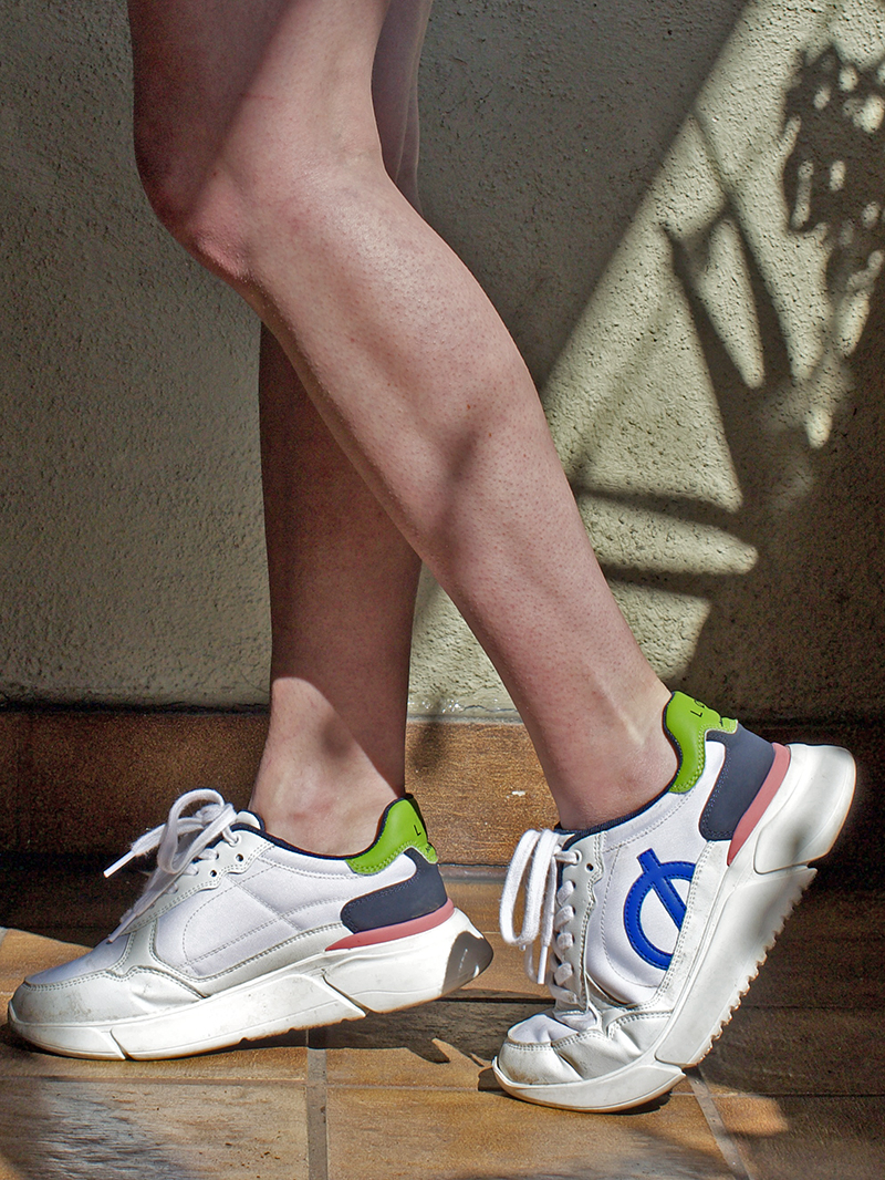 Person wearing white sneakers with colorful accents standing on a wooden floor.