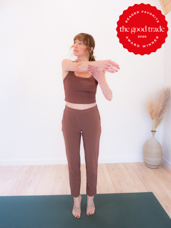 A woman in matching brown workout clothes stretches her arm across her chest on a yoga mat. A red badge in the corner reads “FashionGroomSpot 2023 award winner.”.