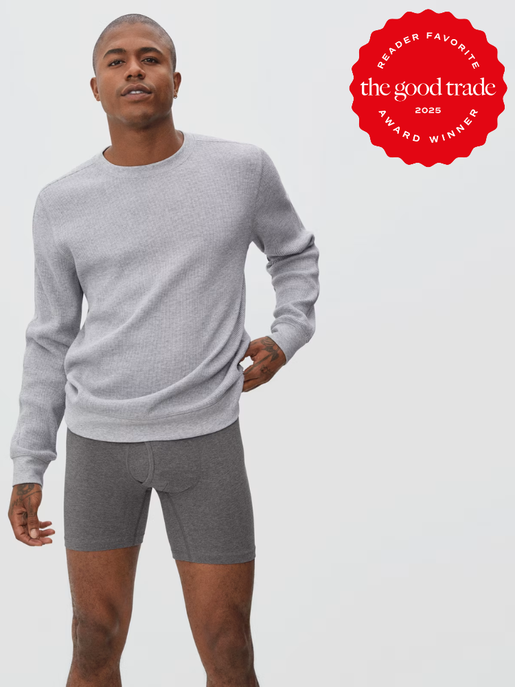 A man wears a light gray long-sleeve shirt and dark gray boxer briefs, standing against a plain background next to a red "FashionGroomSpot 2025 Award Winner" badge.
