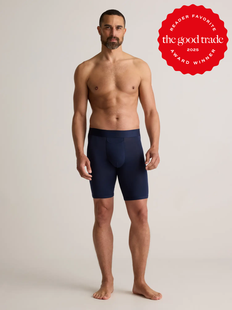 A shirtless man stands facing forward wearing navy blue boxer briefs. A red badge in the upper right corner reads "FashionGroomSpot 2025 Award Winner.